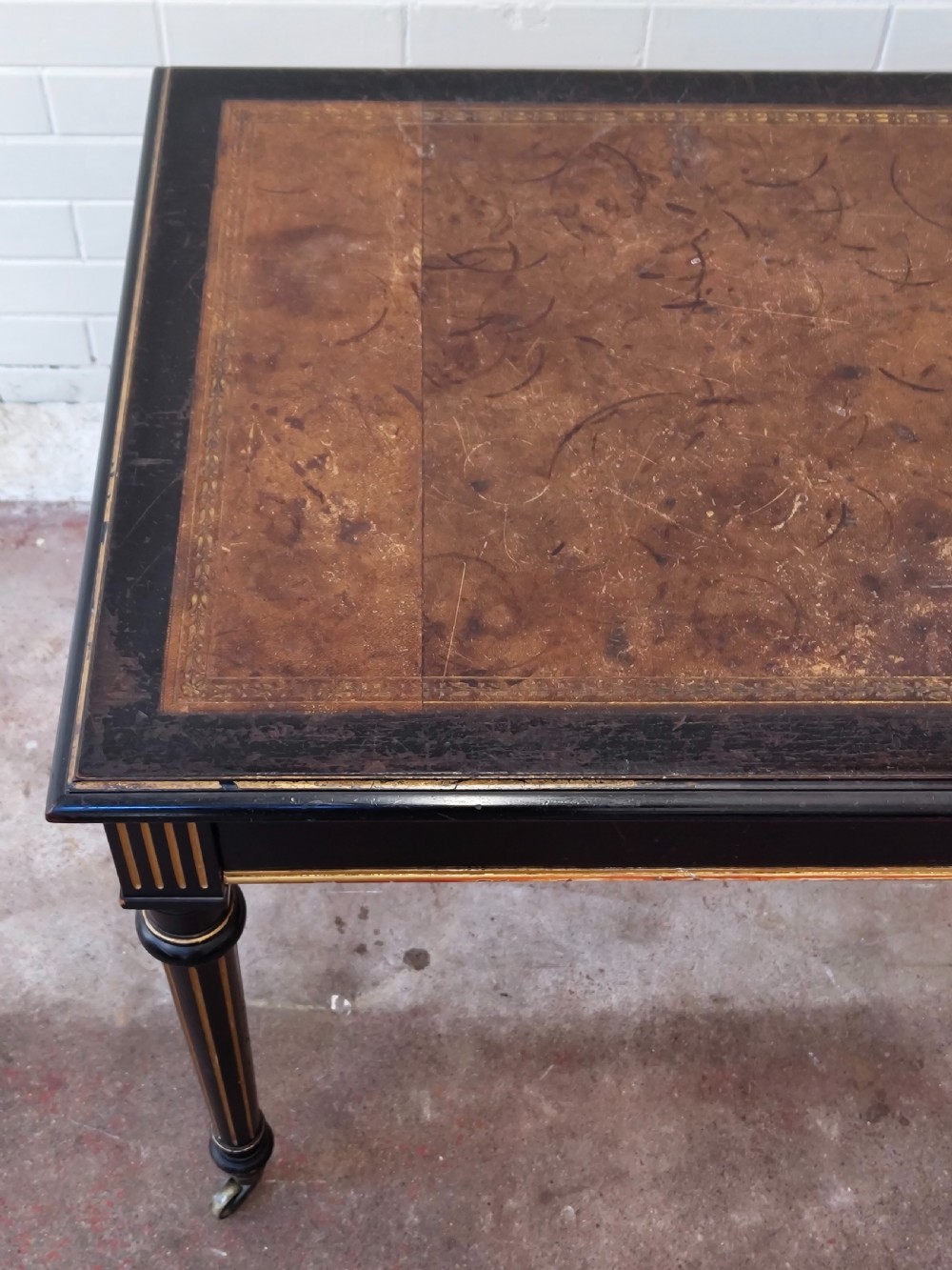 A Victorian Aesthetic Movement ebonised writing table featuring a brown leather inset top, fluted legs with gilt detailing, and brass castors. View IX