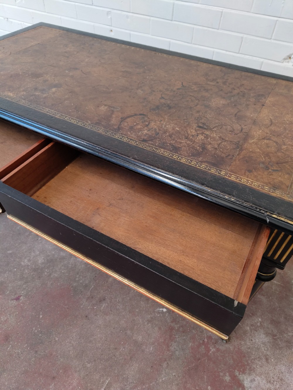 A Victorian Aesthetic Movement ebonised writing table featuring a brown leather inset top, fluted legs with gilt detailing, and brass castors. View XI