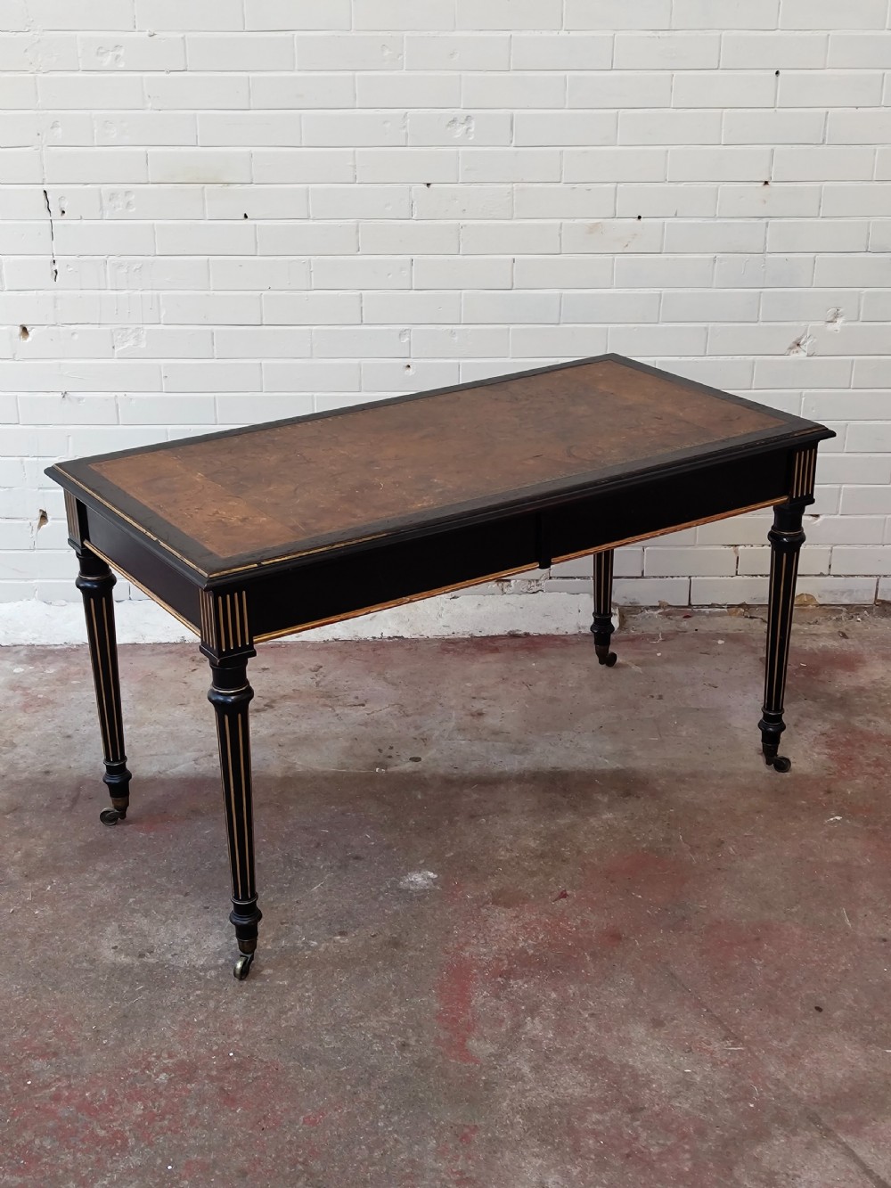 A Victorian Aesthetic Movement ebonised writing table featuring a brown leather inset top, fluted legs with gilt detailing, and brass castors. View XIII