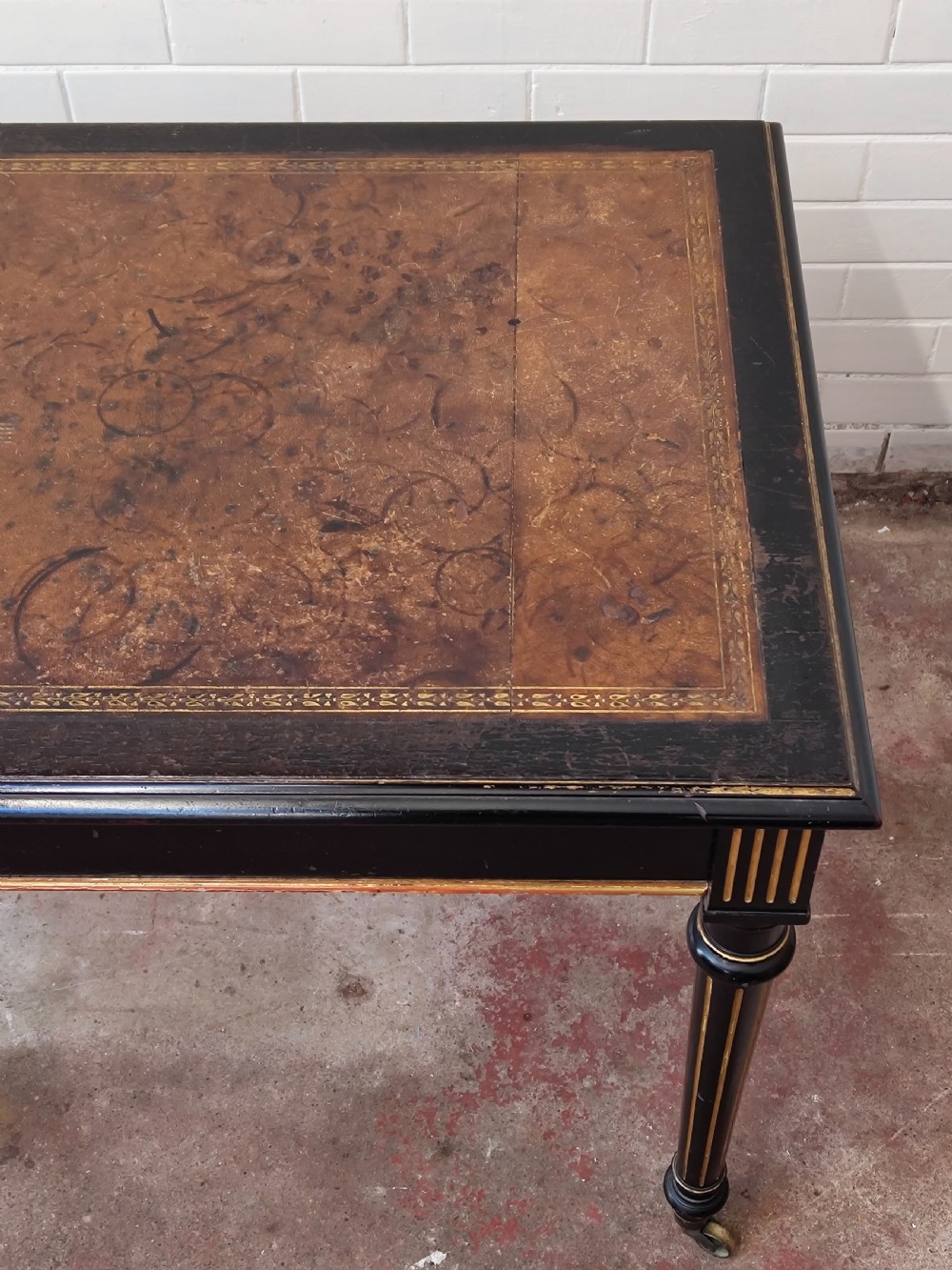 A Victorian Aesthetic Movement ebonised writing table featuring a brown leather inset top, fluted legs with gilt detailing, and brass castors. View XV
