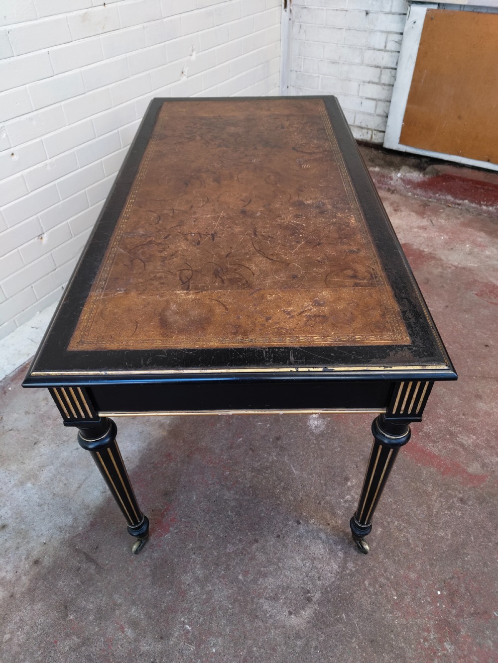 A Victorian Aesthetic Movement ebonised writing table featuring a brown leather inset top, fluted legs with gilt detailing, and brass castors. View XX