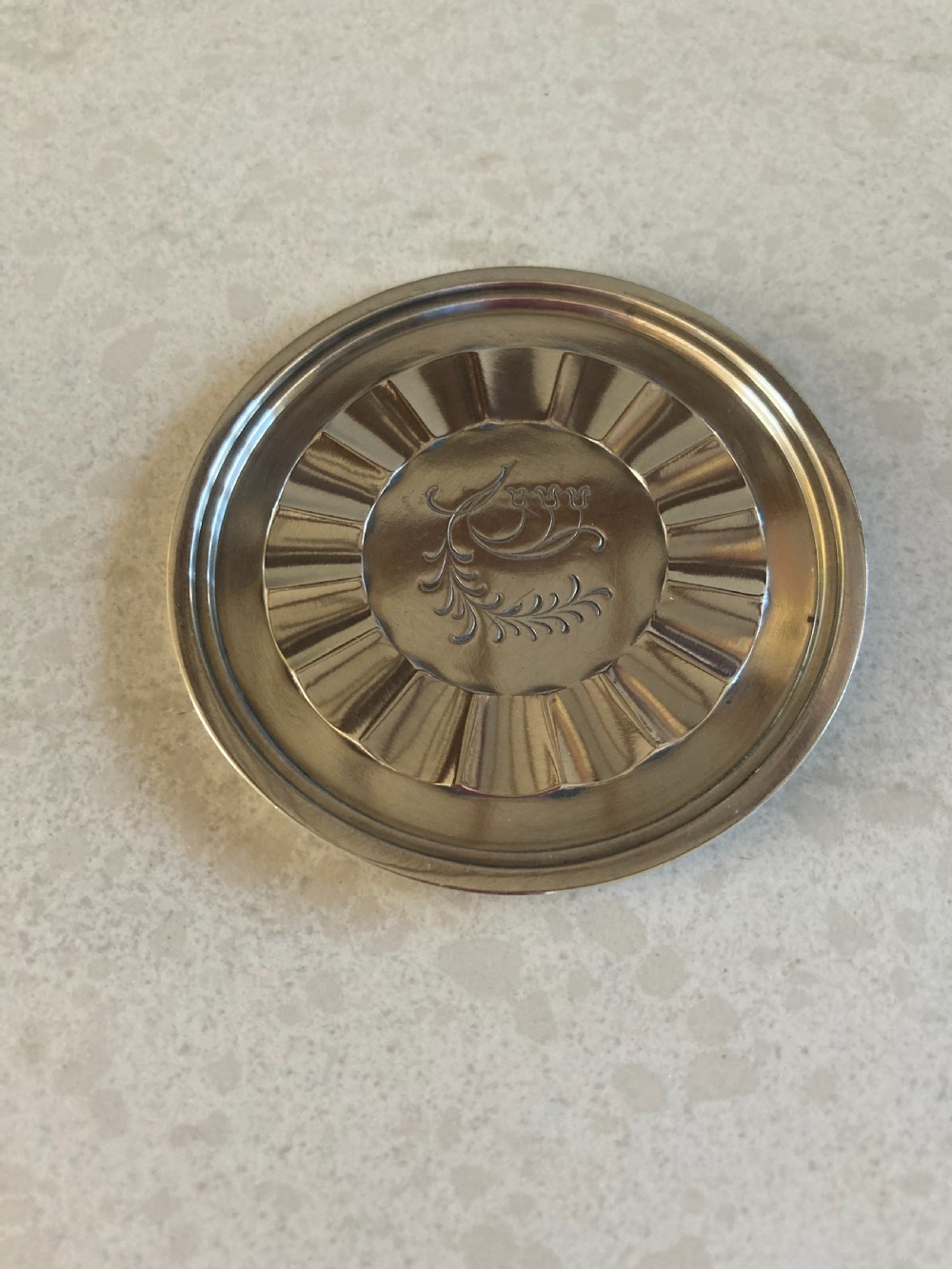 A circular silver coaster featuring a fluted inner rim and an engraved botanical floral design in the centre.