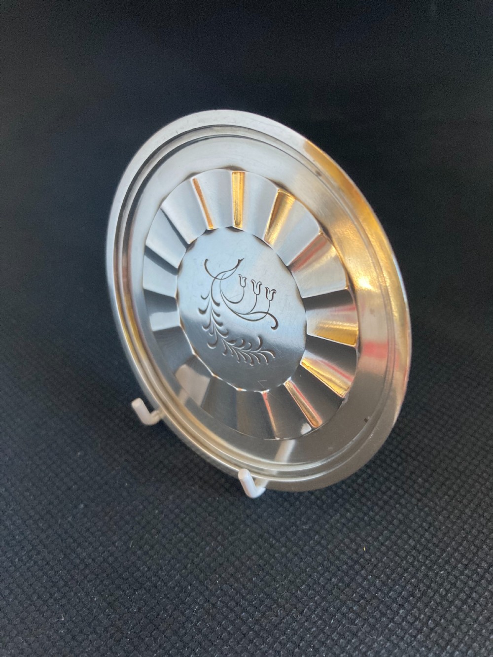 A circular silver coaster featuring a fluted inner rim and an engraved botanical floral design in the centre. View III