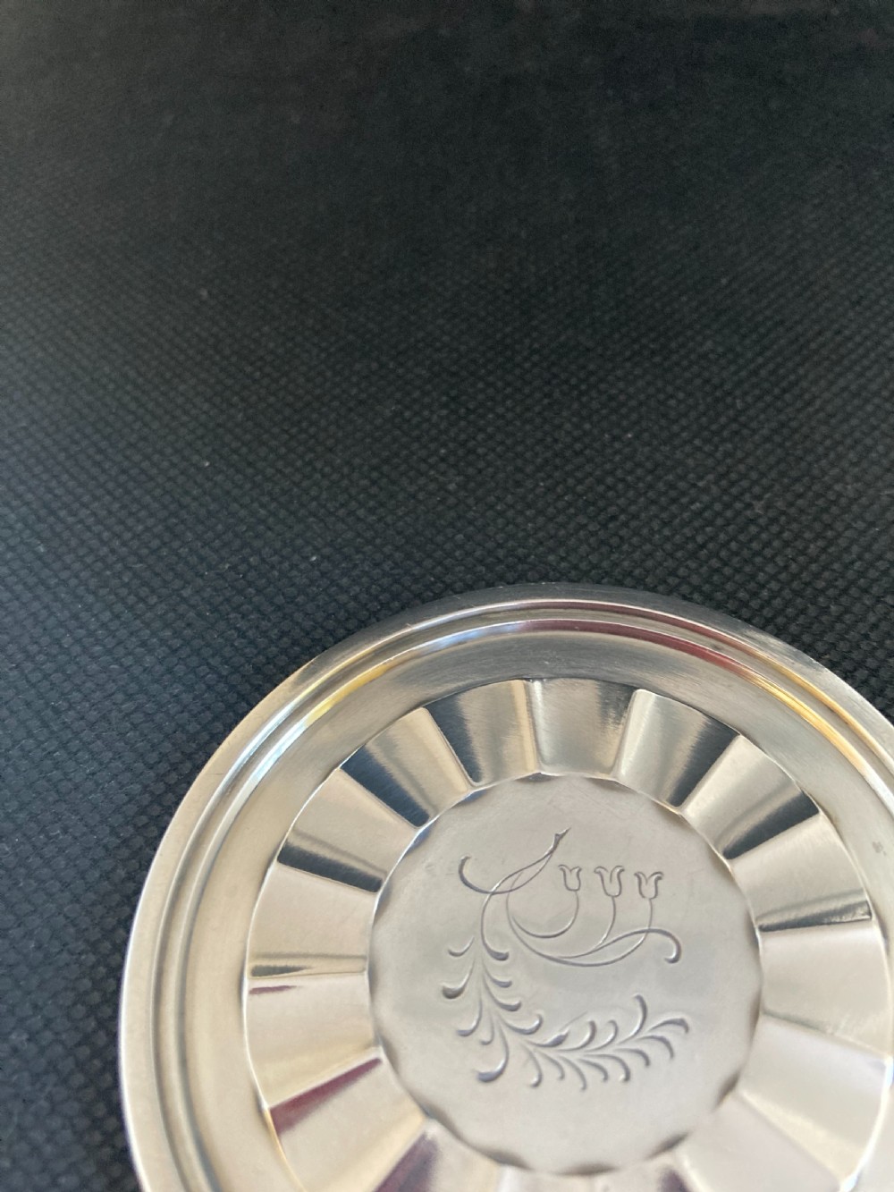 A circular silver coaster featuring a fluted inner rim and an engraved botanical floral design in the centre. View IV