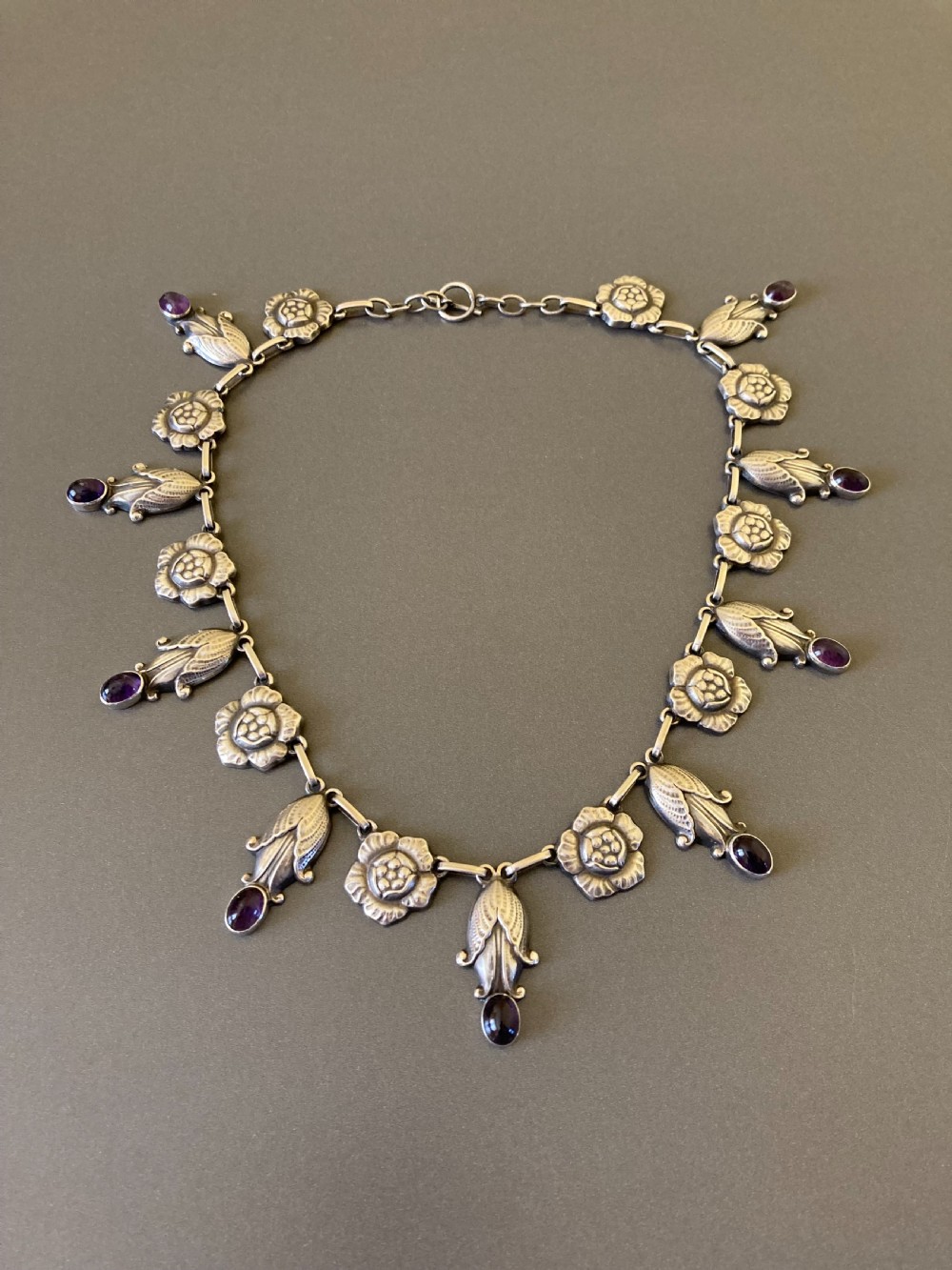 A Danish sterling silver Art Nouveau necklace featuring sculpted floral links and dangling cabochon amethyst gemstones.