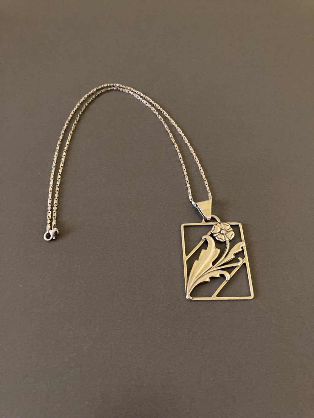 A rectangular silver pendant on a delicate chain featuring an openwork floral and leaf design.