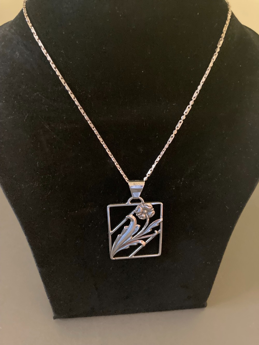A rectangular silver pendant on a delicate chain featuring an openwork floral and leaf design. View III