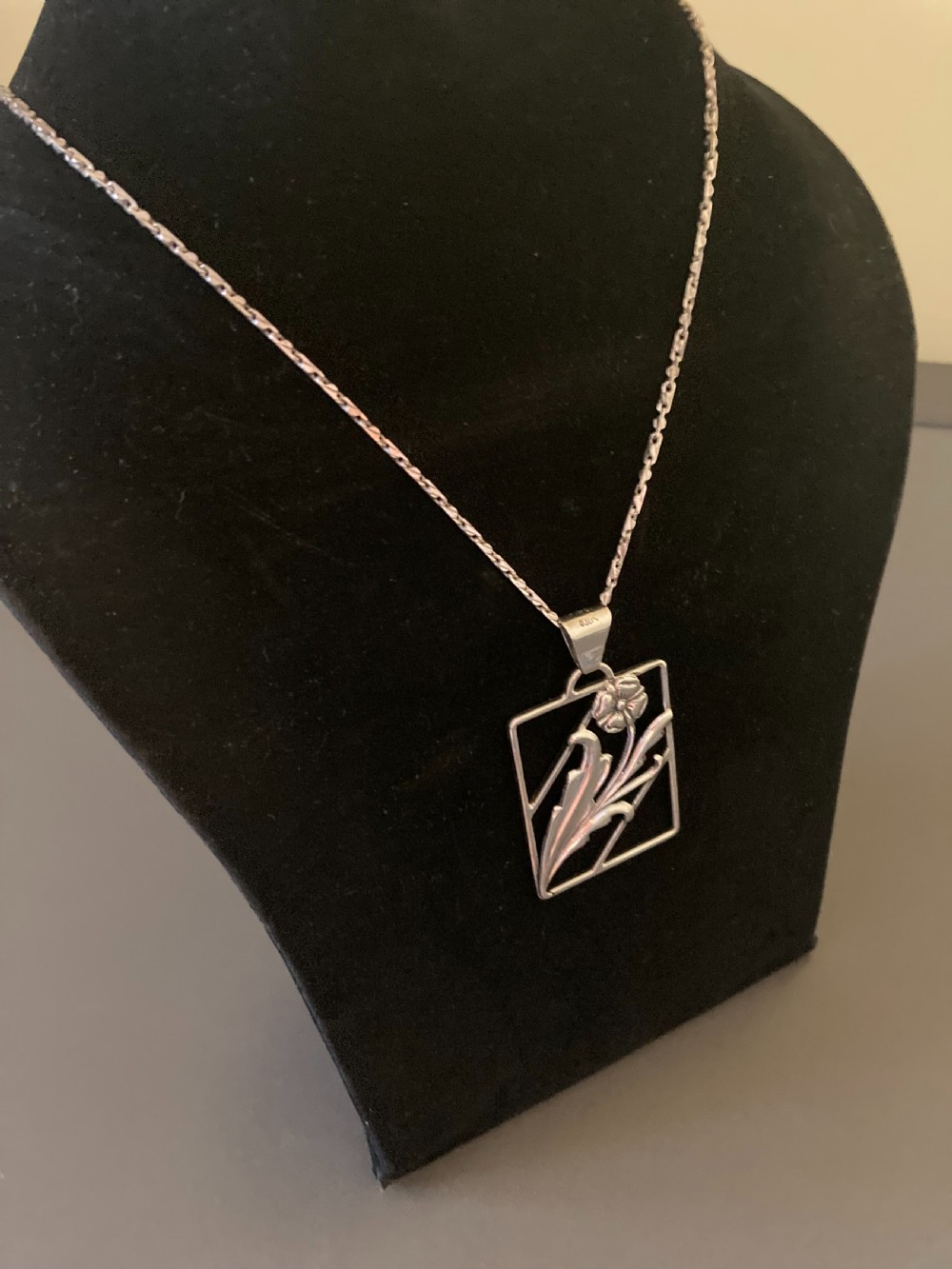 A rectangular silver pendant on a delicate chain featuring an openwork floral and leaf design. View IV