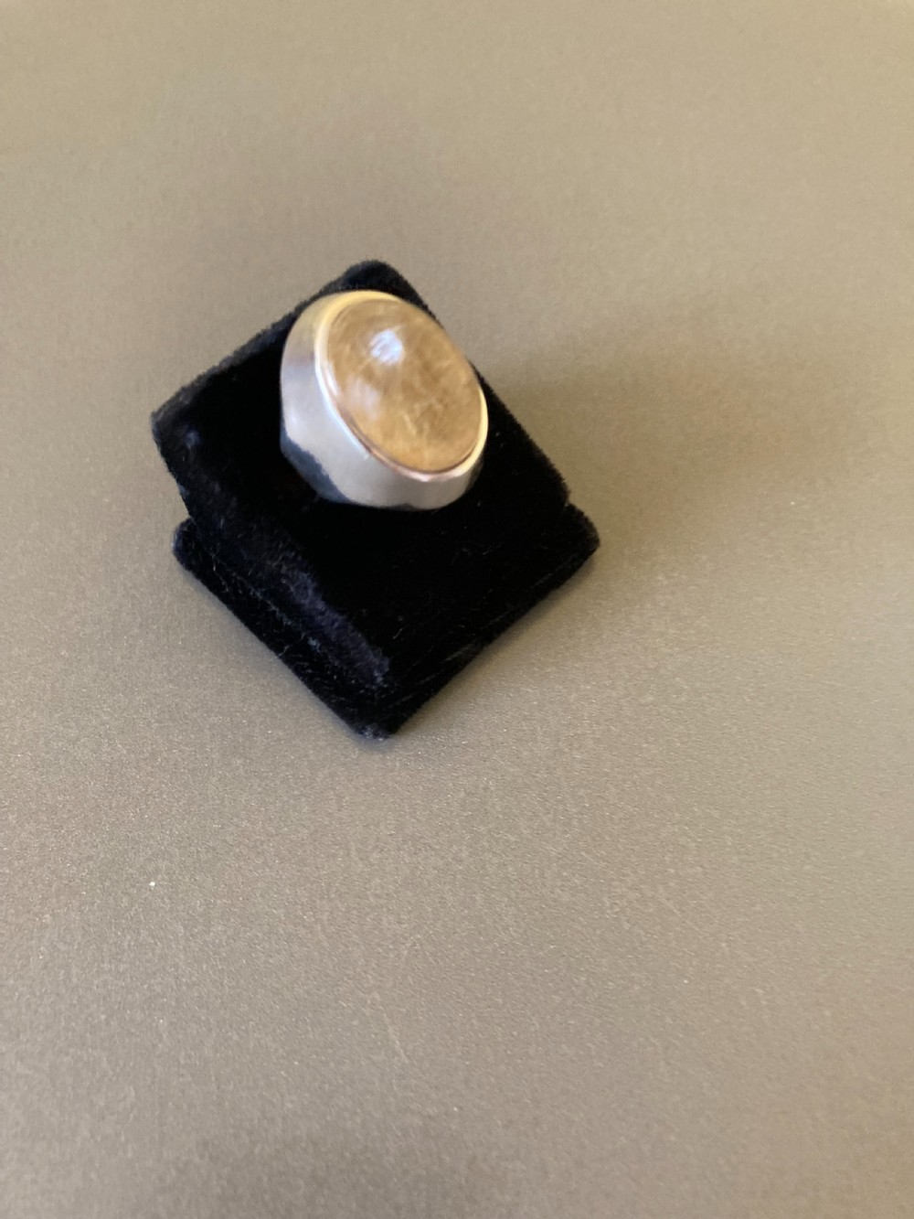 A close-up shot of a vintage Danish silver ring featuring a smooth, domed rutilated quartz gemstone set in a heavy sterling silver band, resting on a small clear acrylic display stand. View III