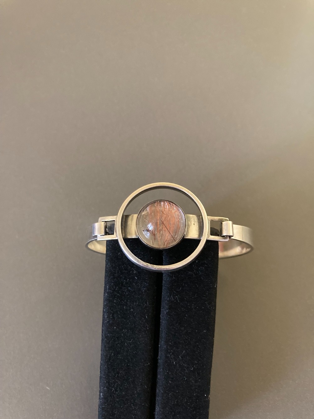 A hinged silver bangle features a central circular frame holding a cabochon rutilated quartz gemstone with needle-like inclusions. View III