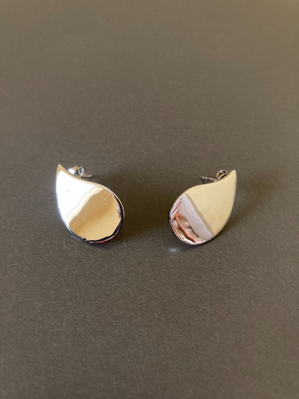 A pair of polished silver teardrop earrings resting inside a red presentation box. View II