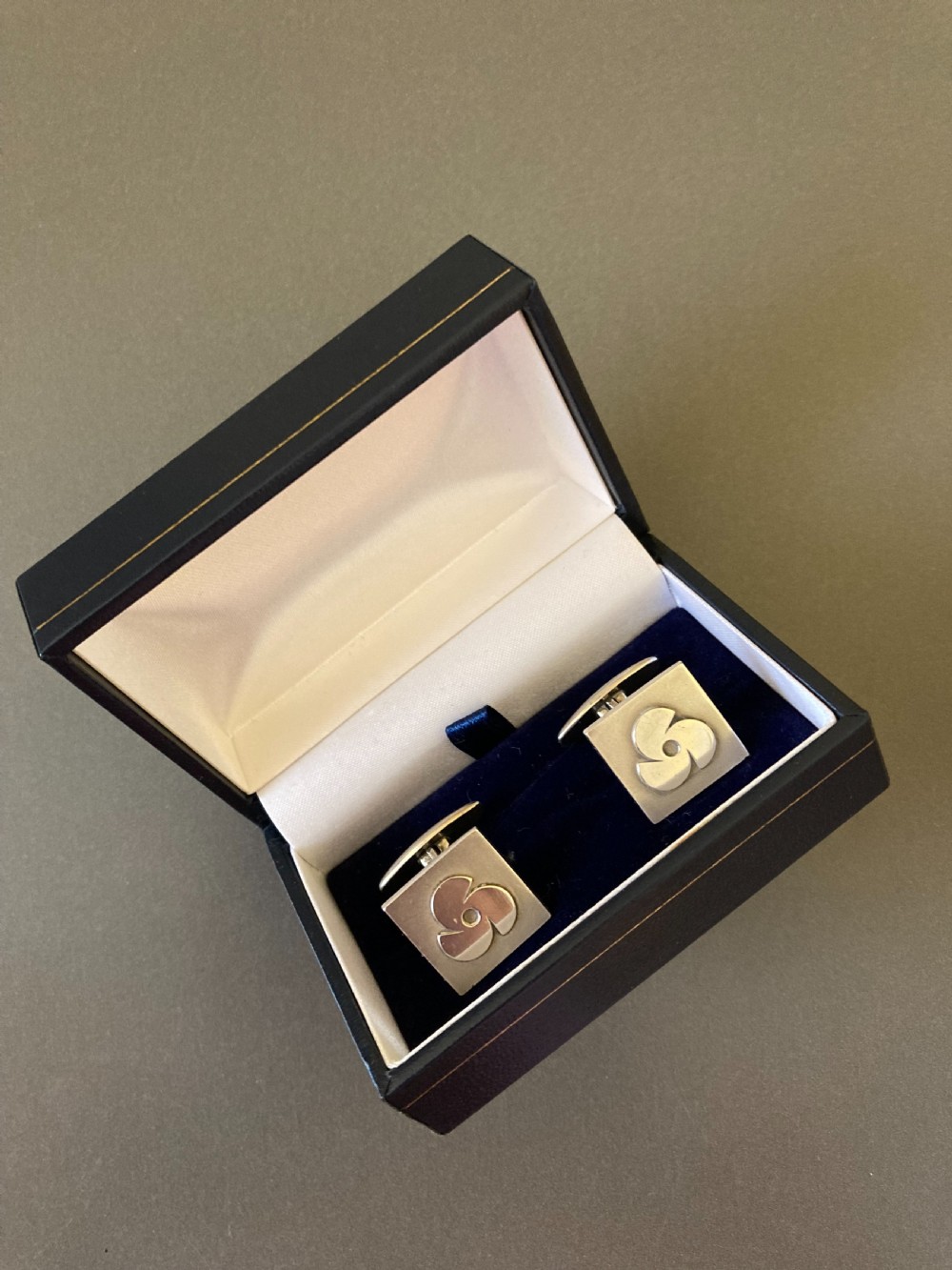 A pair of square Danish silver cufflinks featuring an abstract geometric pinwheel design, displayed in a dark hinged presentation box. View V