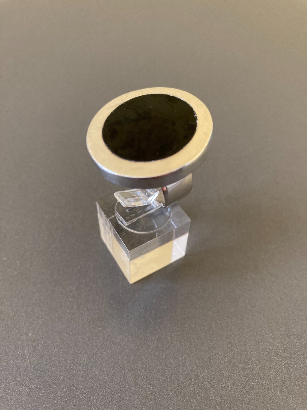 A round vintage Danish sterling silver ring featuring a central disc of black enamel, displayed inside a clear plastic ring box. View IV