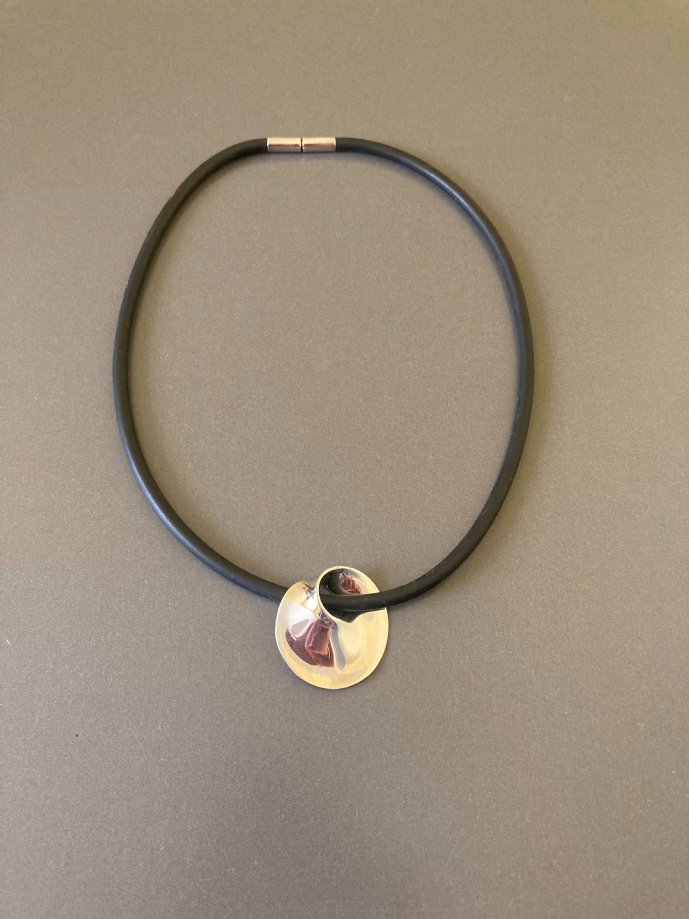 A vintage Georg Jensen sterling silver Moebius pendant threaded on a dark rubber cord against a neutral grey background.