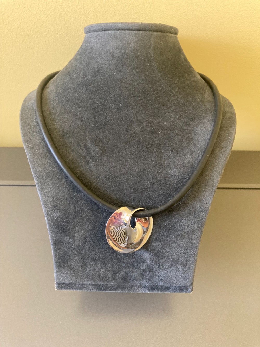 A vintage Georg Jensen sterling silver Moebius pendant threaded on a dark rubber cord against a neutral grey background. View IV