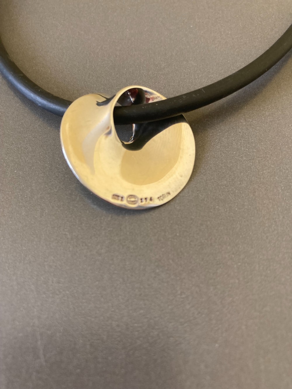 A vintage Georg Jensen sterling silver Moebius pendant threaded on a dark rubber cord against a neutral grey background. View VI