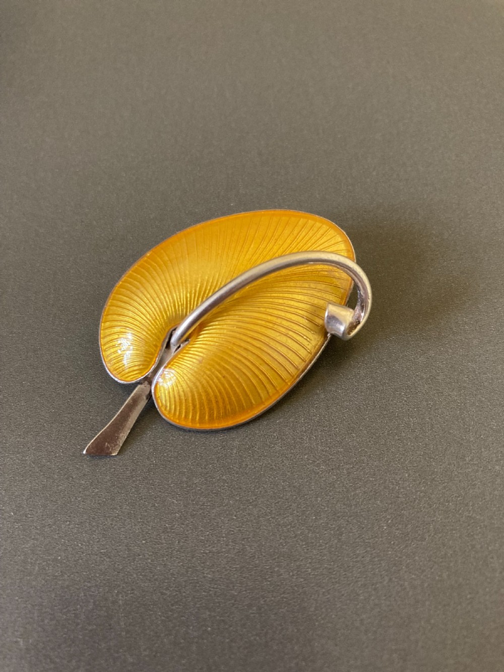 A yellow guilloche enamel leaf brooch set in sterling silver, featuring a stem and curved vein detail.
