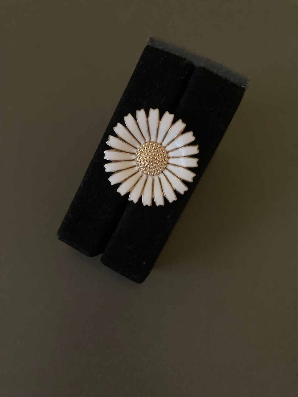 A close-up shot of a round silver and white enamel daisy brooch featuring textured gilt metal details at the centre. View II