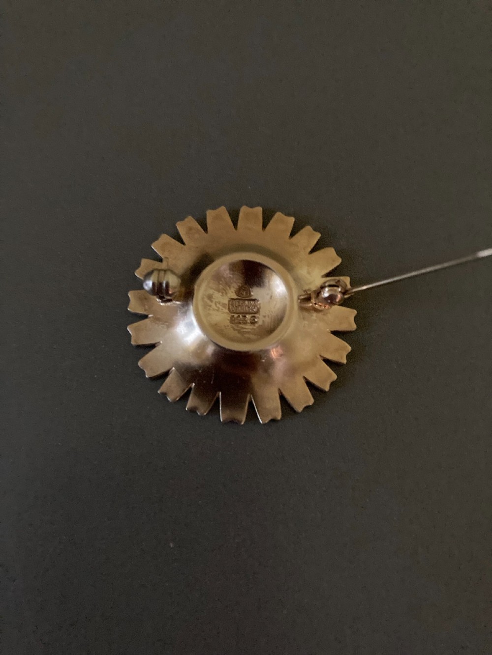 A close-up shot of a round silver and white enamel daisy brooch featuring textured gilt metal details at the centre. View III