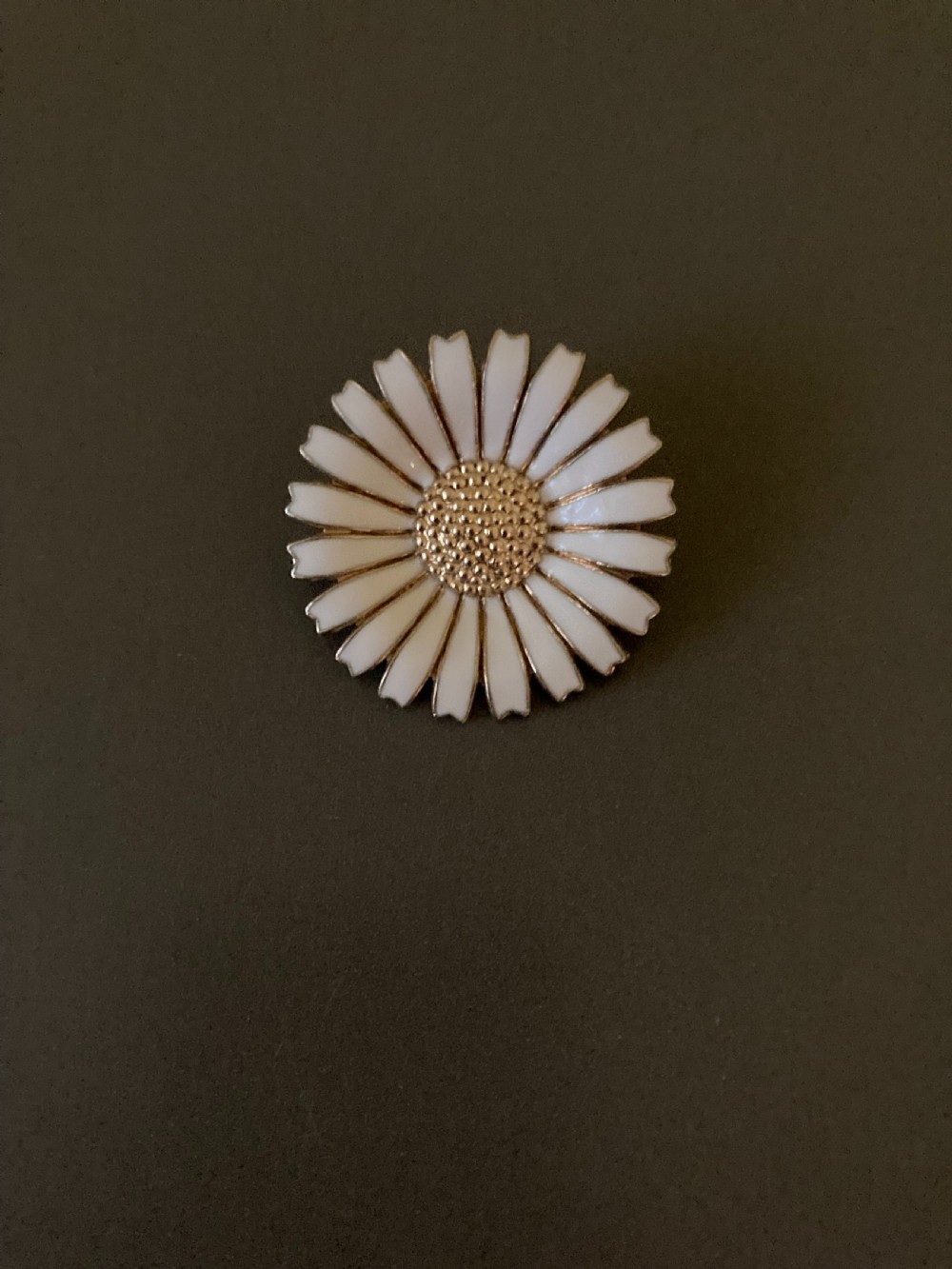A close-up shot of a round silver and white enamel daisy brooch featuring textured gilt metal details at the centre. View IV