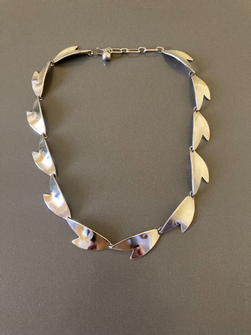 An articulated sterling silver necklace composed of linked leaf-shaped modernist plates against a neutral background.