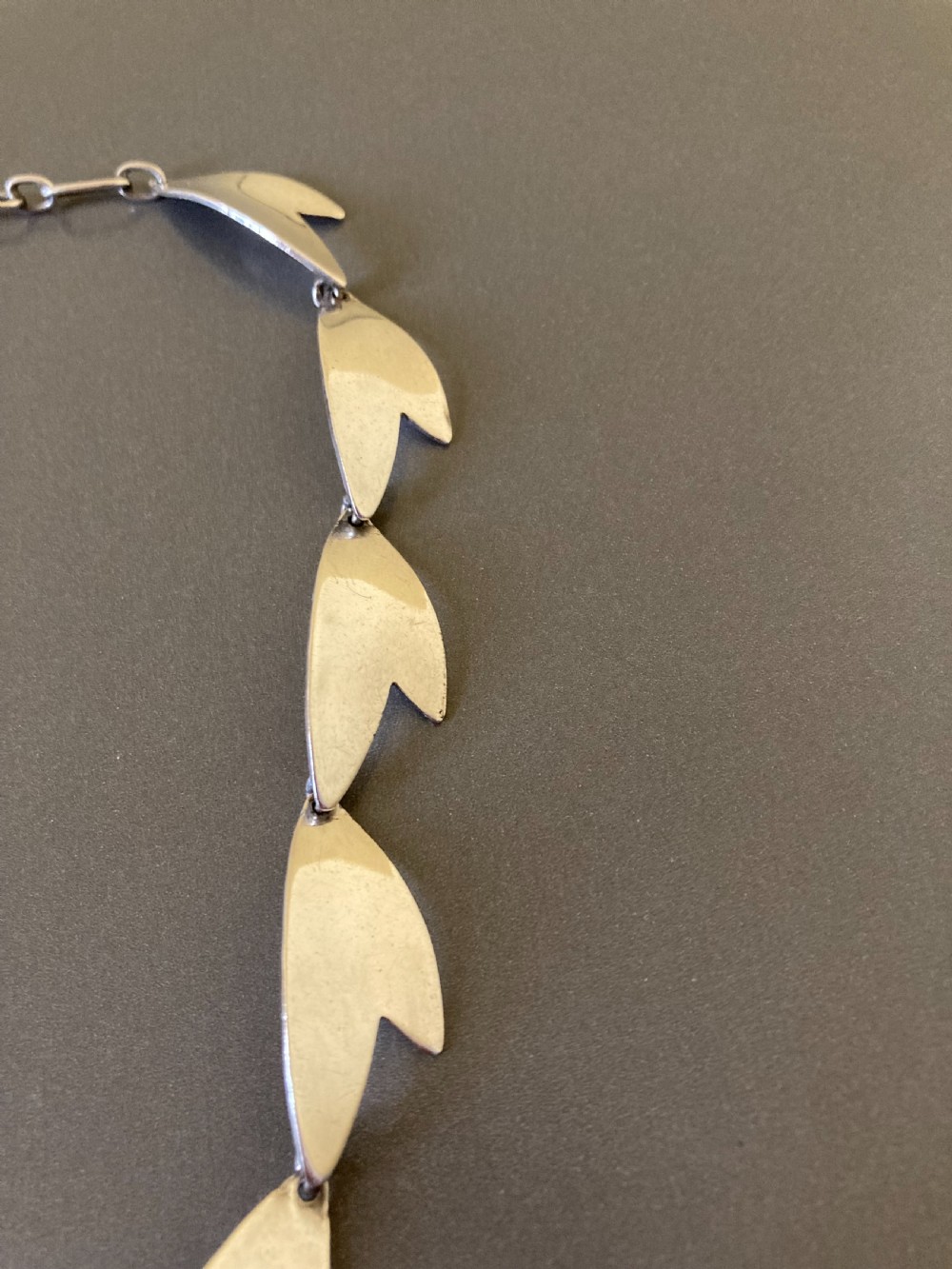 An articulated sterling silver necklace composed of linked leaf-shaped modernist plates against a neutral background. View II