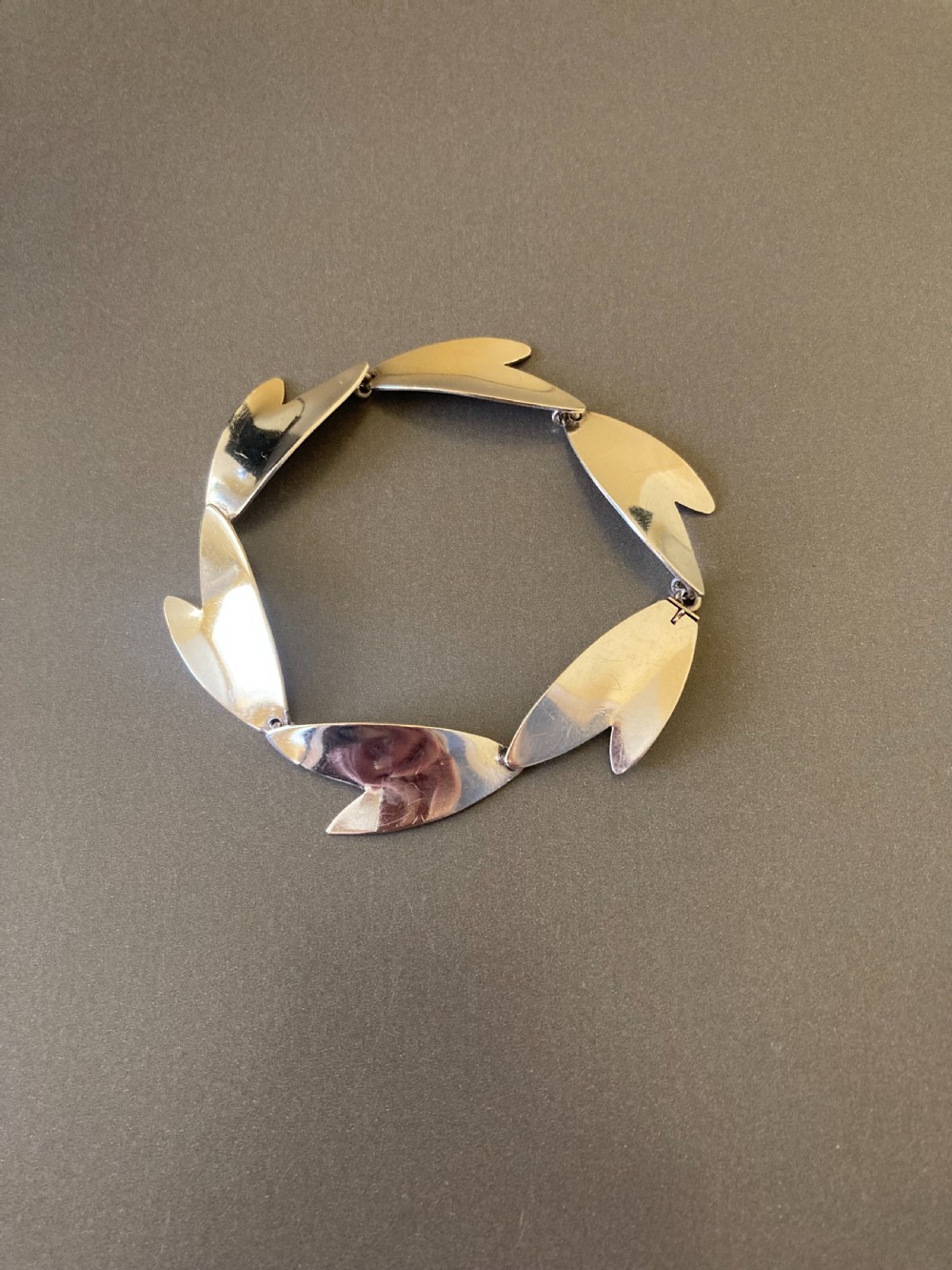An overhead view of a linked silver bracelet featuring geometric petal-shaped components arranged in a linear sequence on a neutral grey background. View II