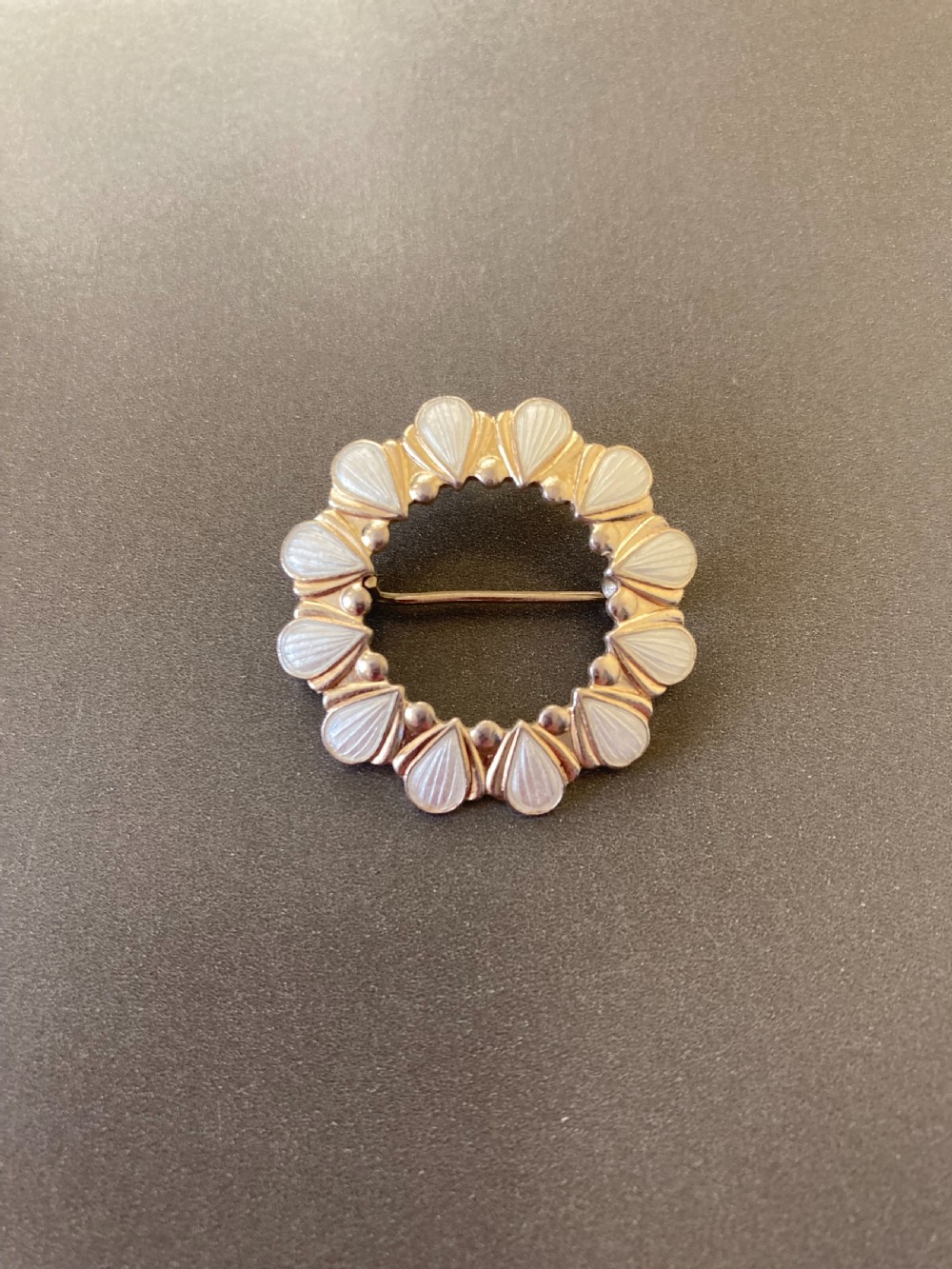 A circular vintage Danish silver gilt brooch featuring a repeating pattern of white enamel teardrop elements.