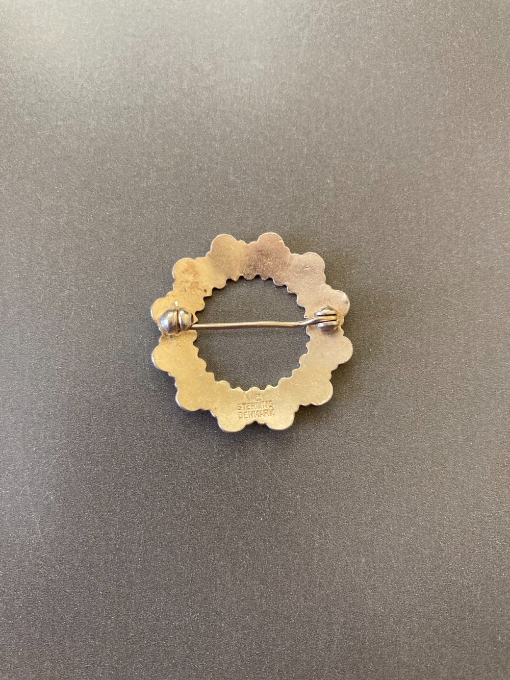 A circular vintage Danish silver gilt brooch featuring a repeating pattern of white enamel teardrop elements. View IV