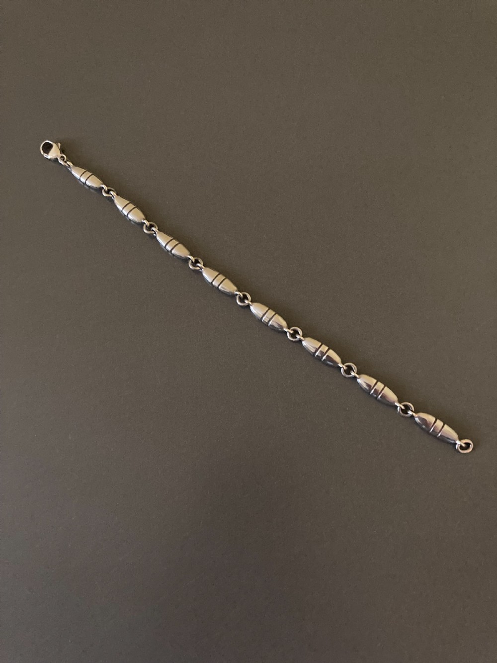 A vintage Georg Jensen sterling silver link bracelet featuring elongated bullet-shaped segments connected by small rings against a dark grey background.