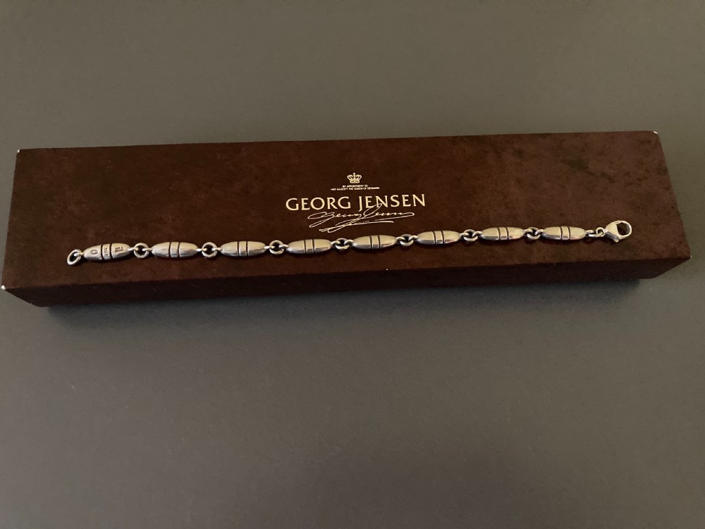 A vintage Georg Jensen sterling silver link bracelet featuring elongated bullet-shaped segments connected by small rings against a dark grey background. View V