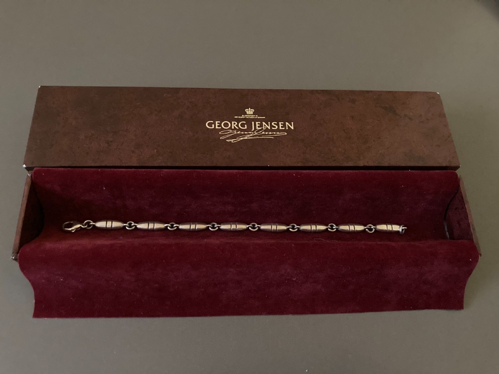 A vintage Georg Jensen sterling silver link bracelet featuring elongated bullet-shaped segments connected by small rings against a dark grey background. View VII