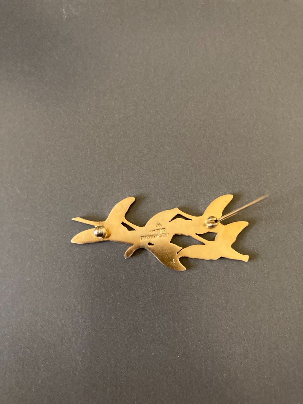 An overhead view of a vintage silver gilt and white enamel brooch depicting stylised flying birds. View III
