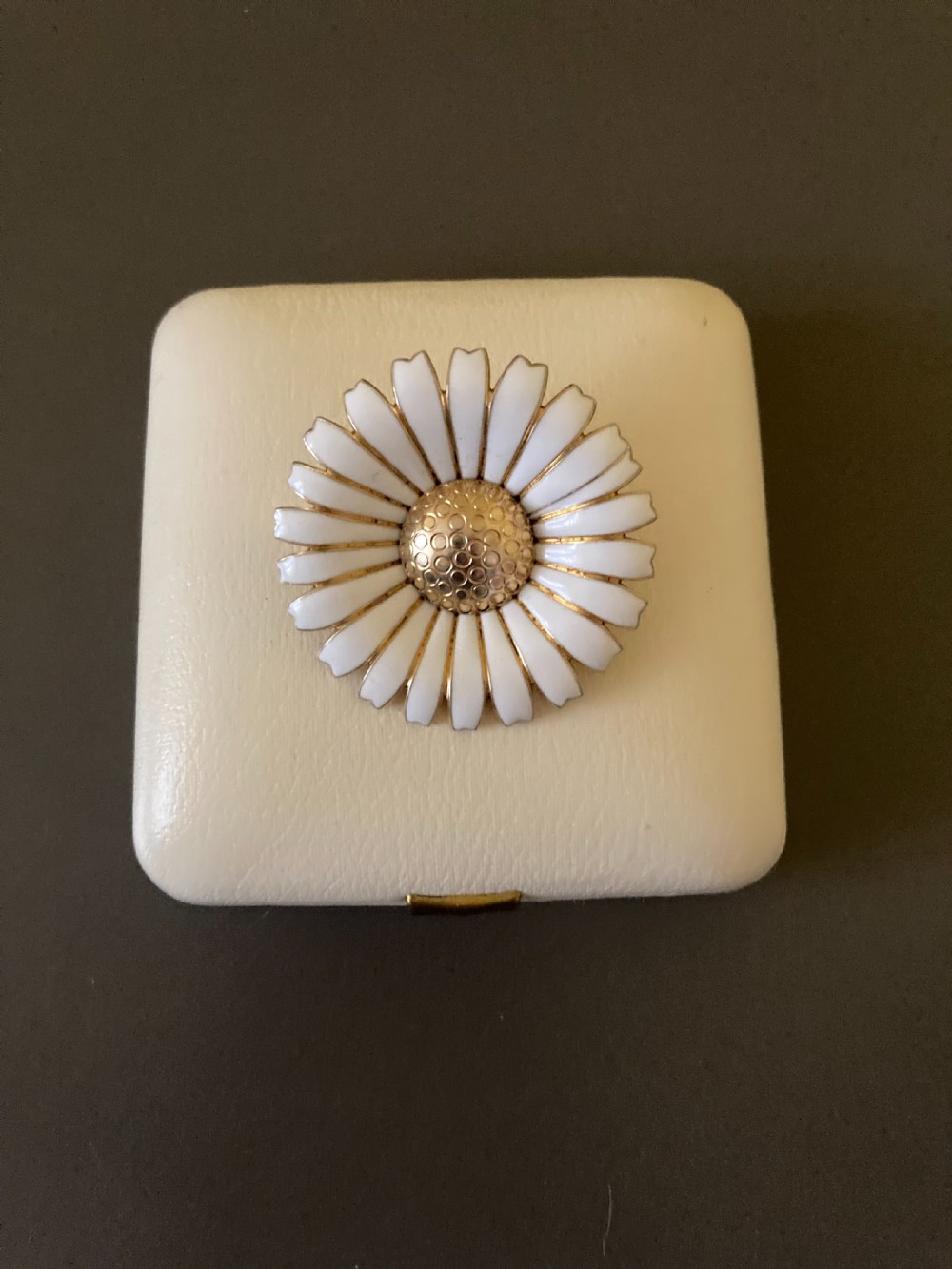 A circular vintage brooch in the shape of a white daisy with a gold-textured centre. View VI