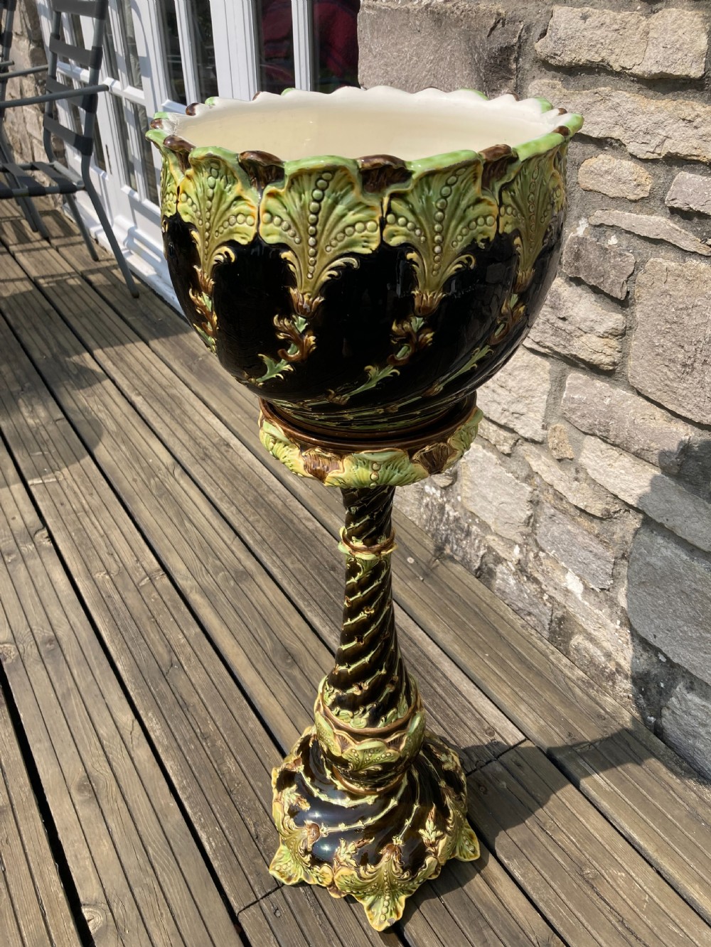 An Art Nouveau majolica ceramic jardiniere resting on a tall twisted pedestal stand decorated with dark brown glaze and raised green acanthus leaf relief motifs.