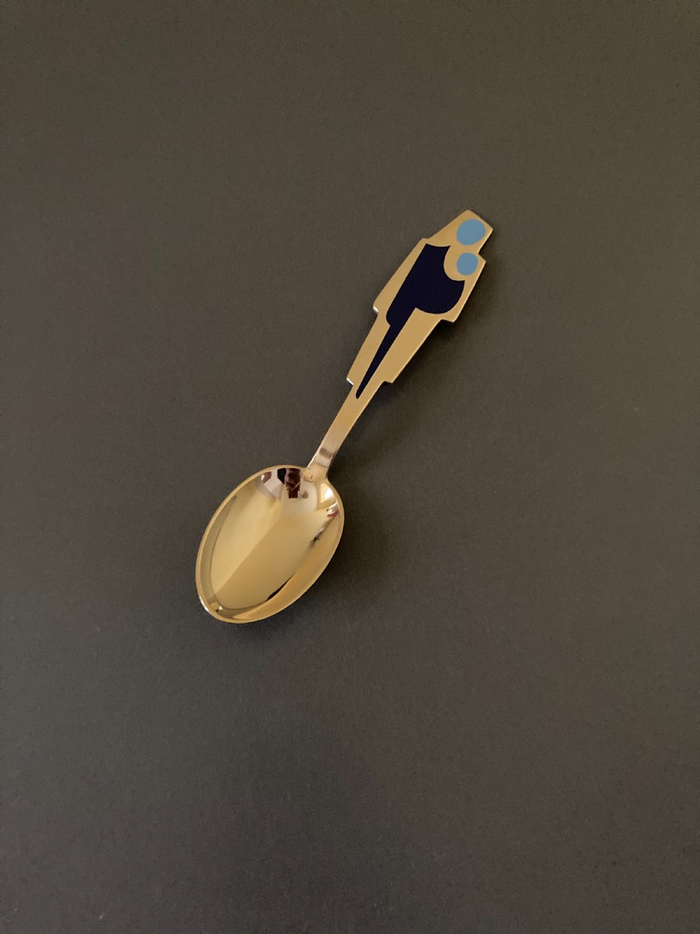 A gold gilt sterling silver spoon featuring a stylized blue enamel abstract design on the handle, dating from 1962.