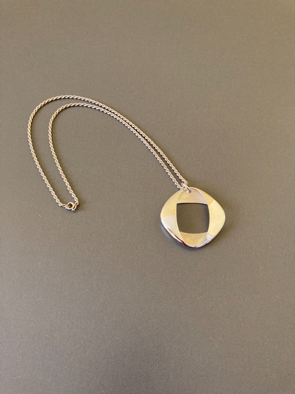 A sterling silver geometric open square pendant designed by Henning Koppel resting on a silver chain against a grey background.