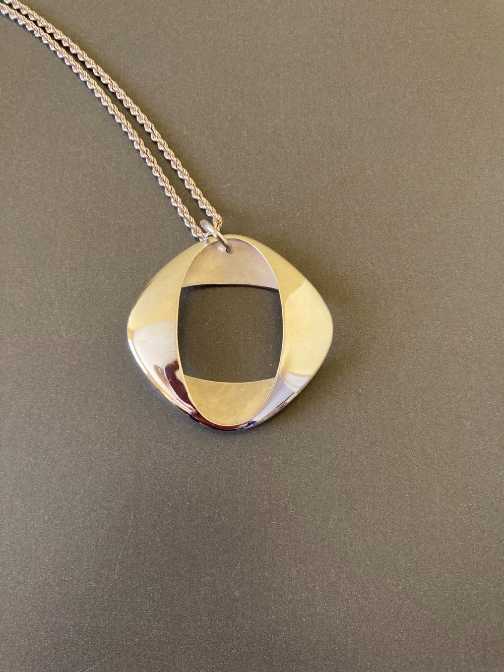 A sterling silver geometric open square pendant designed by Henning Koppel resting on a silver chain against a grey background. View II