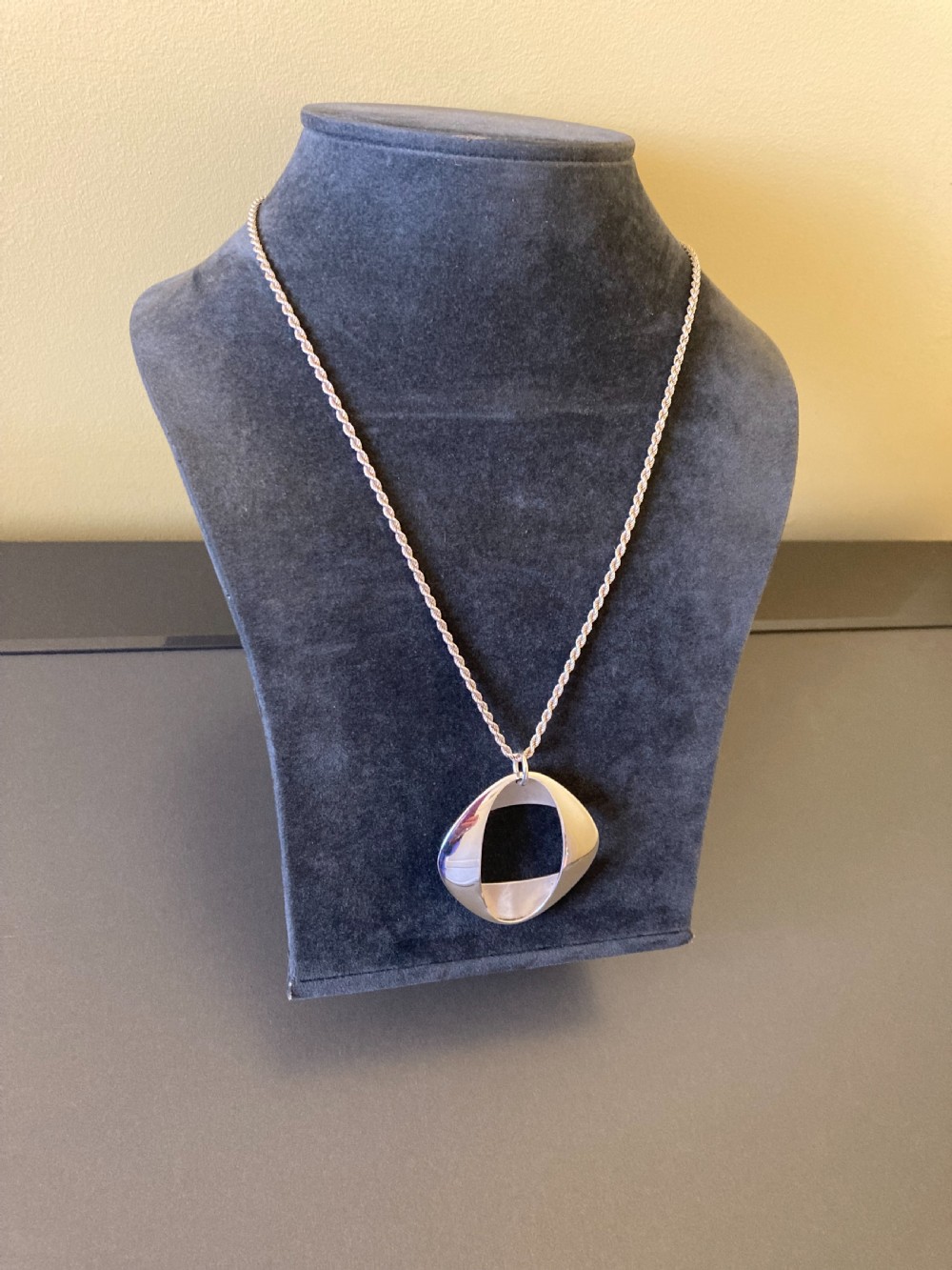 A sterling silver geometric open square pendant designed by Henning Koppel resting on a silver chain against a grey background. View III