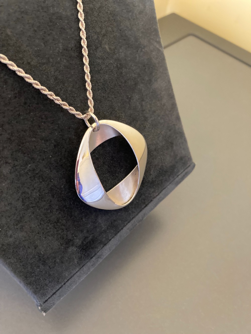 A sterling silver geometric open square pendant designed by Henning Koppel resting on a silver chain against a grey background. View IV