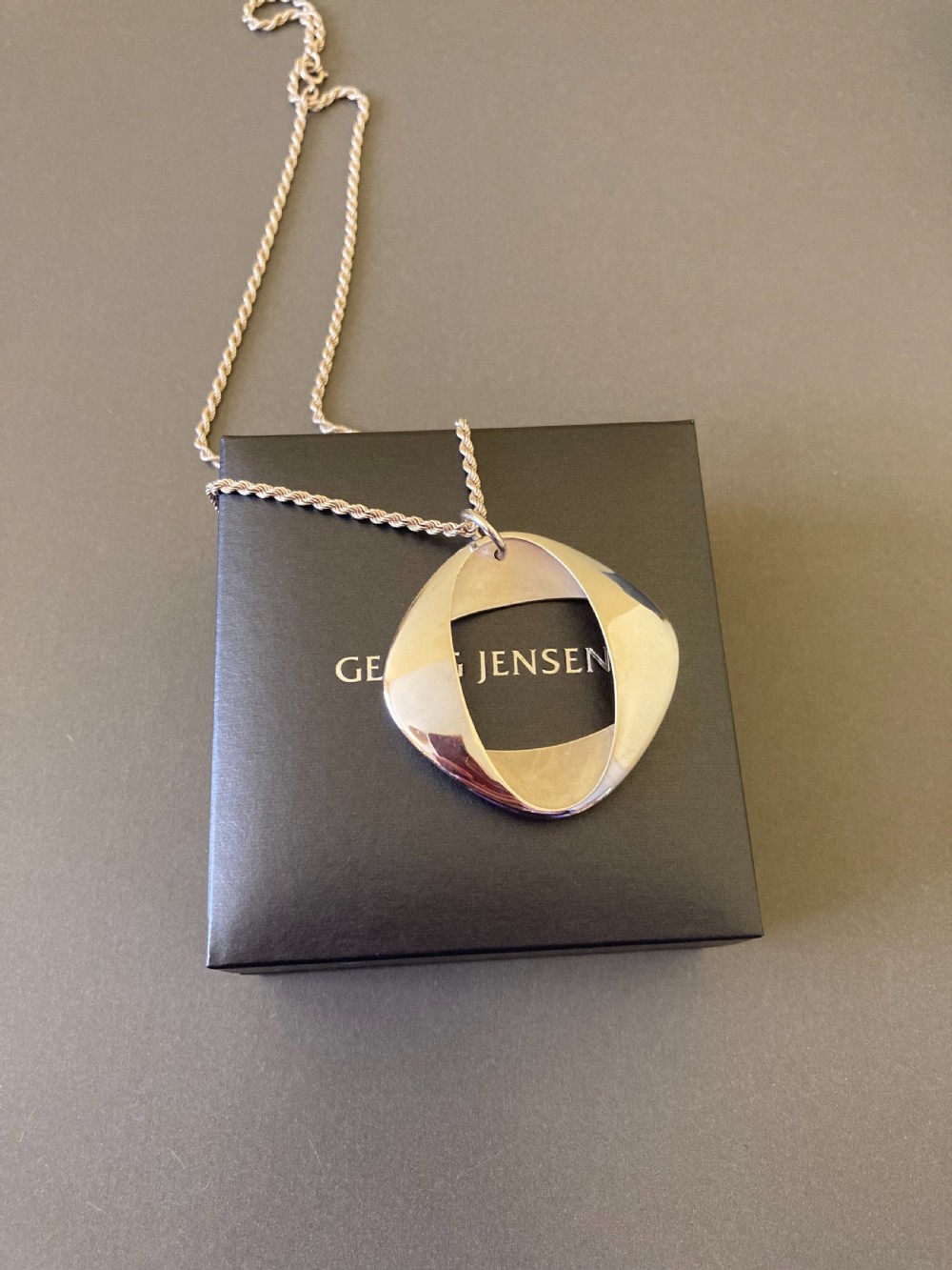 A sterling silver geometric open square pendant designed by Henning Koppel resting on a silver chain against a grey background. View VI