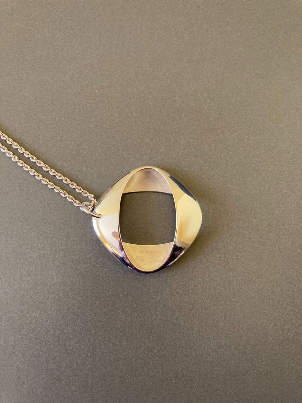 A sterling silver geometric open square pendant designed by Henning Koppel resting on a silver chain against a grey background. View VII