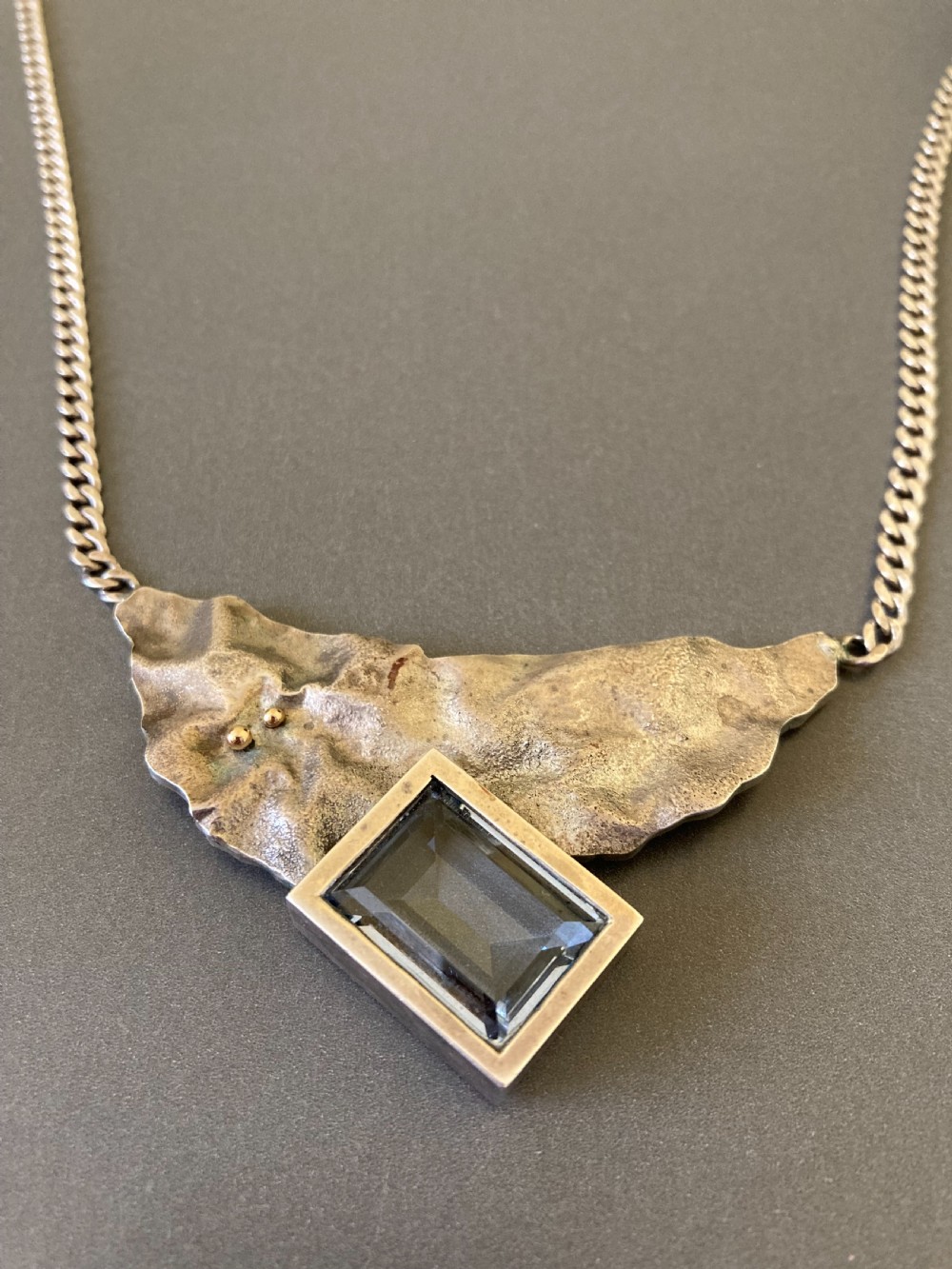 A 1960s sterling silver curb chain necklace featuring a textured asymmetrical pendant with an emerald-cut blue topaz stone. View II