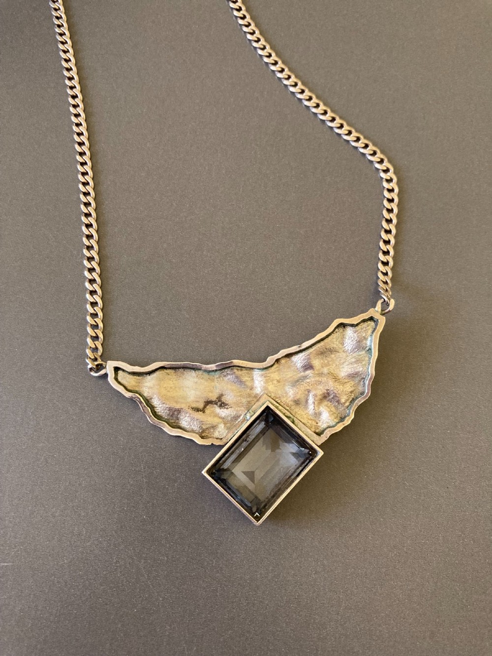 A 1960s sterling silver curb chain necklace featuring a textured asymmetrical pendant with an emerald-cut blue topaz stone. View V