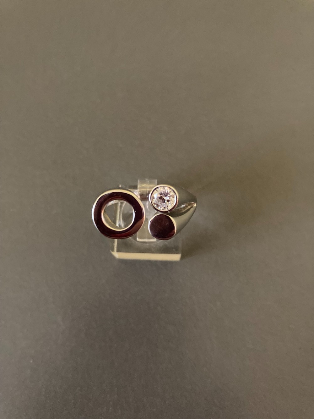 A Danish sterling silver ring from the 1960s featuring an asymmetrical modernist design with an open circle motif, a polished solid disc, and a bezel-set round zirconia stone.
