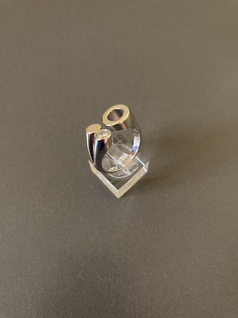 A Danish sterling silver ring from the 1960s featuring an asymmetrical modernist design with an open circle motif, a polished solid disc, and a bezel-set round zirconia stone. View II