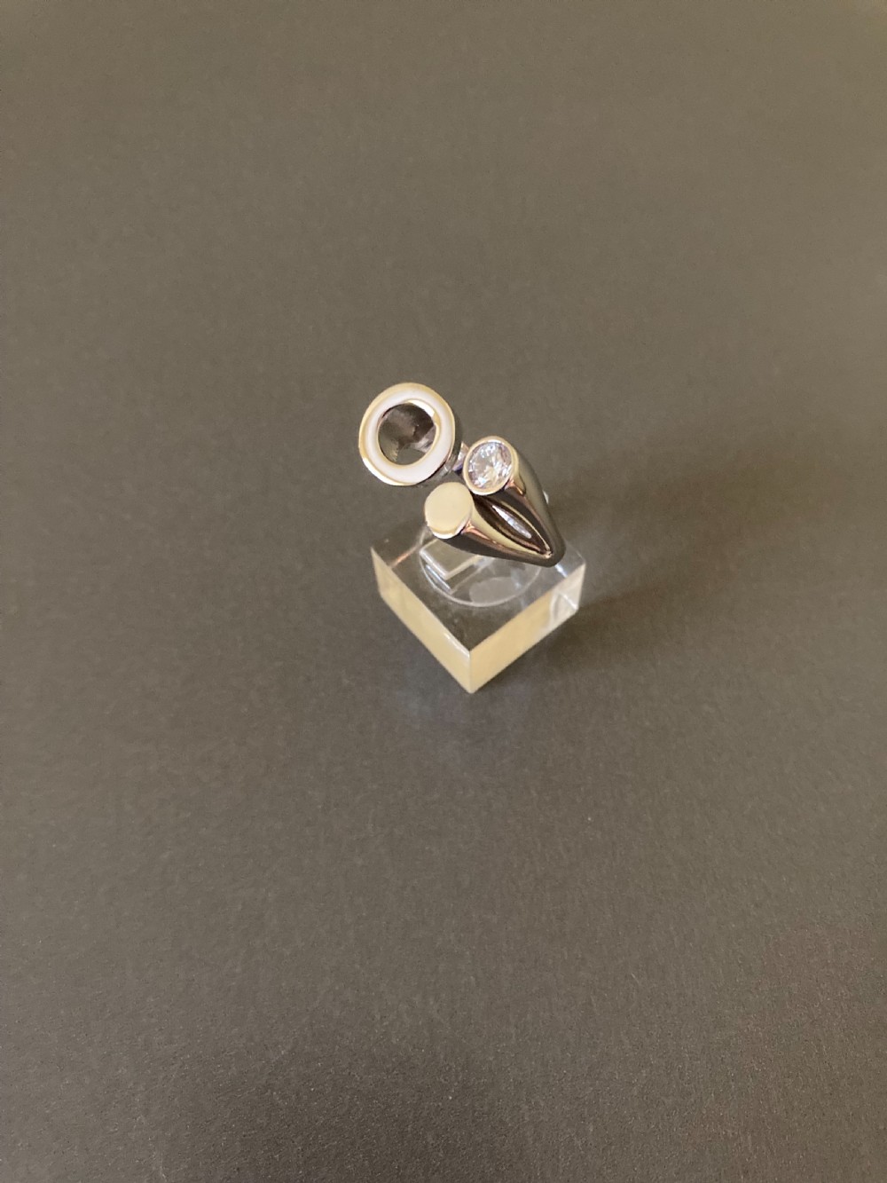 A Danish sterling silver ring from the 1960s featuring an asymmetrical modernist design with an open circle motif, a polished solid disc, and a bezel-set round zirconia stone. View III