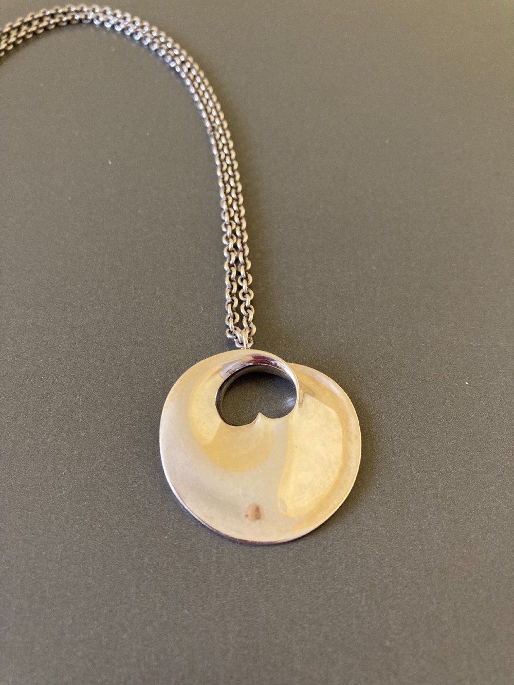 A sterling silver circular pendant featuring an organic cutout design attached to a double fine silver chain.