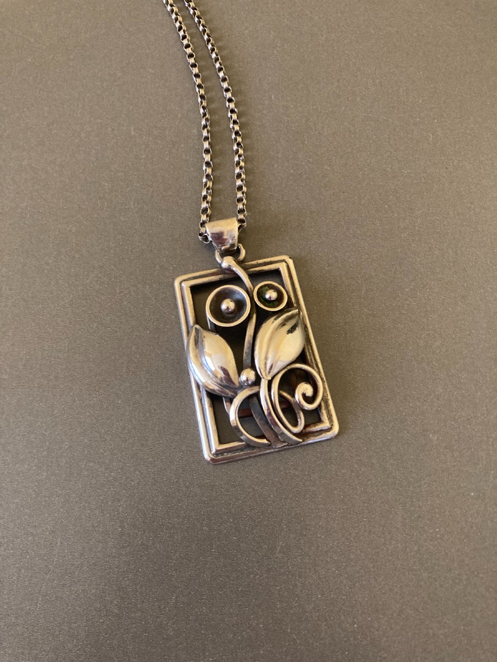 A rectangular sterling silver pendant featuring openwork foliage motifs on a thin silver link chain.