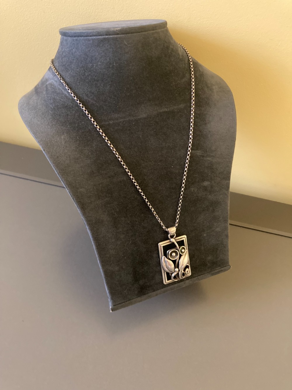 A rectangular sterling silver pendant featuring openwork foliage motifs on a thin silver link chain. View IV